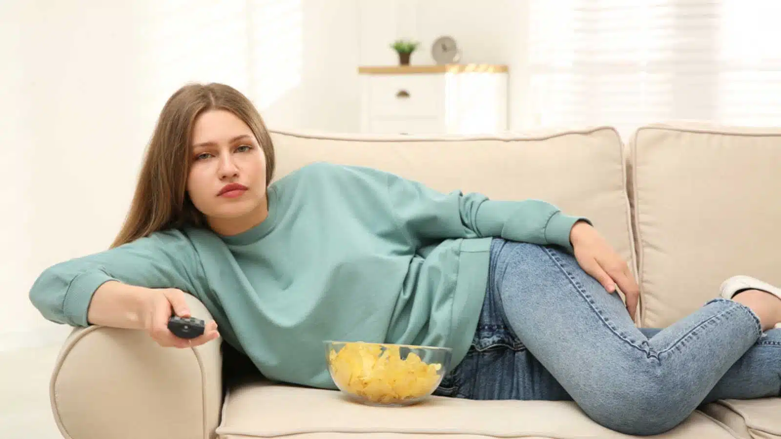 Woman lying in sofa watching tv sadly
