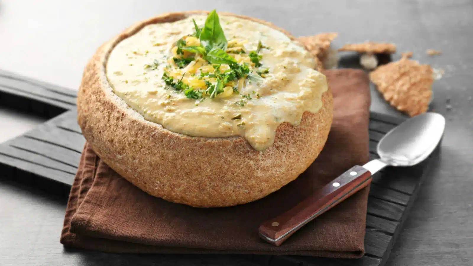 Broccoli cheddar soup in bread bowl on wooden board