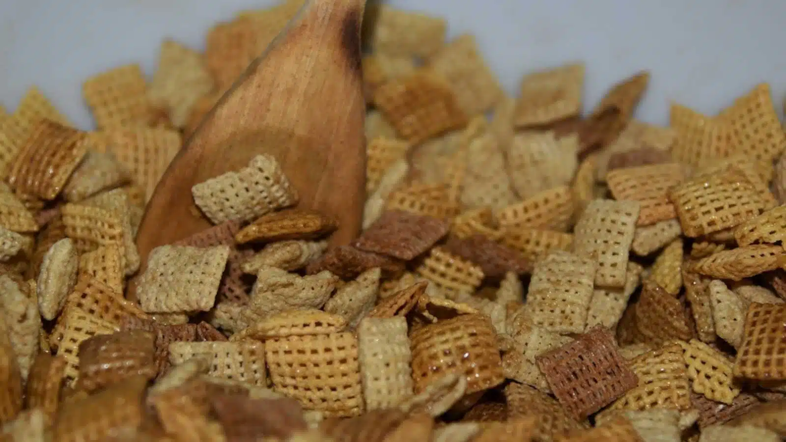 Chex mix being made in a mixing bowl with a wooden spoon